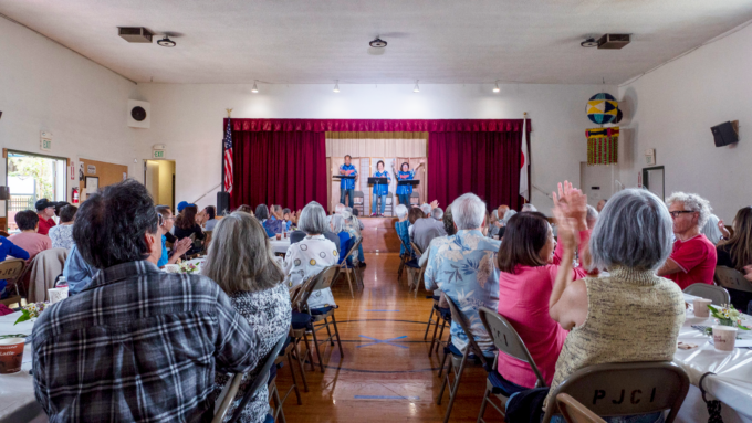 room filled with people watching singers on a stage