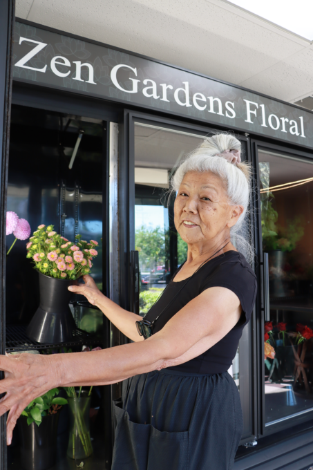 woman florist posing in front refrigerator with sign that says "Zen Gardens Floral"