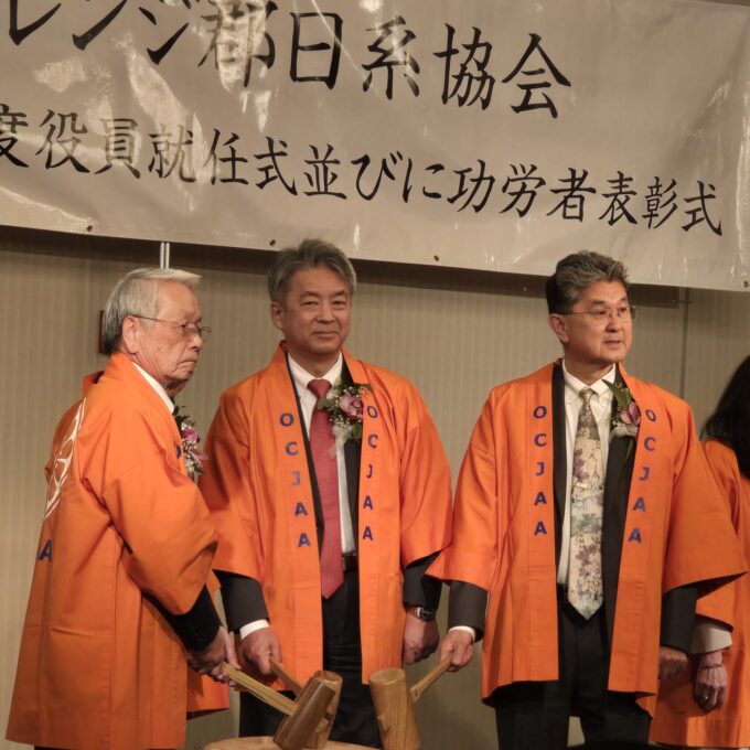 three men in orange happi coats that say "OCJAA"