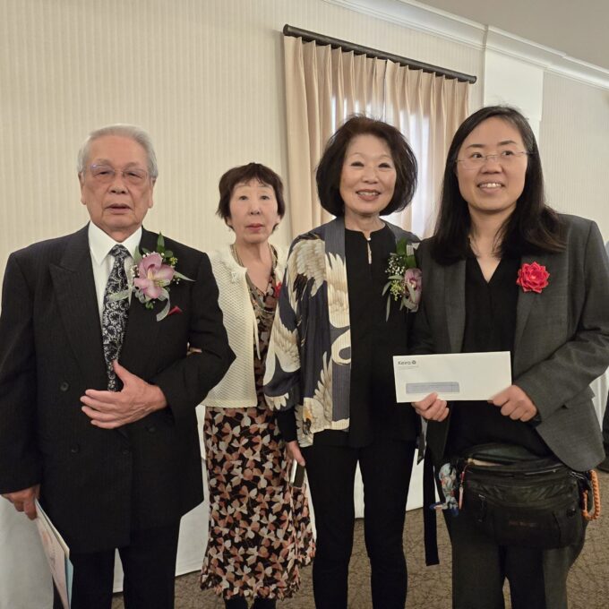 Four people smiling and one person is holding up a envelope