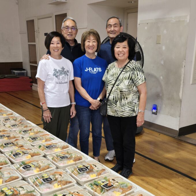five people smiling with rows of bento on table