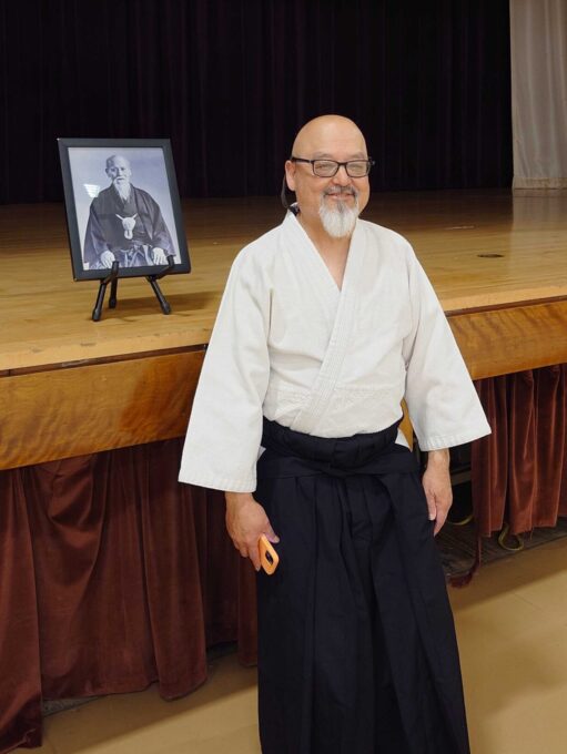 man smiling wearing Aikido gi with photo frame behind him