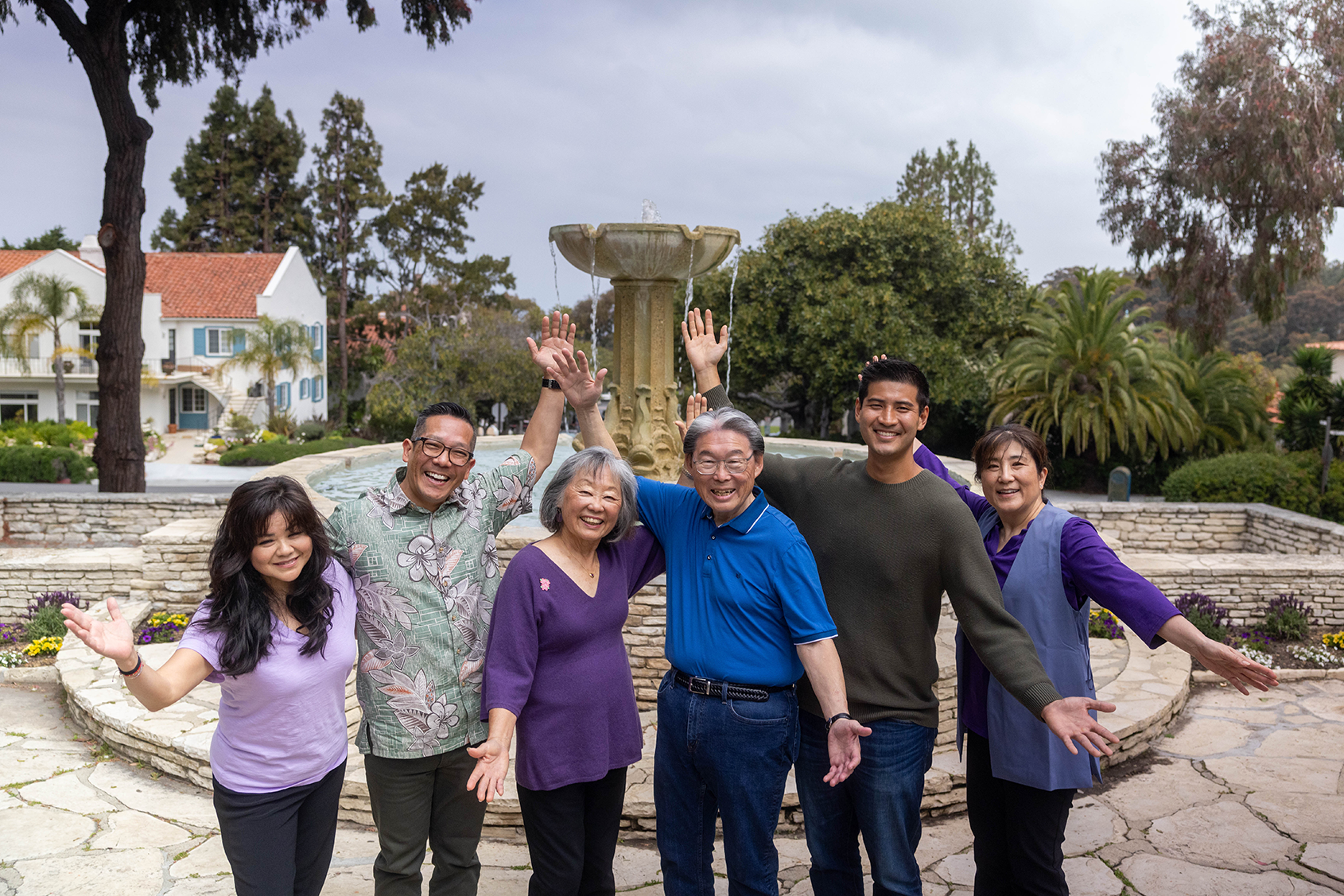group of size people smiling in front of a water fountain with their arms up