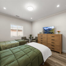 two beds with green comforters, wooden dresser, tv, in a bedroom