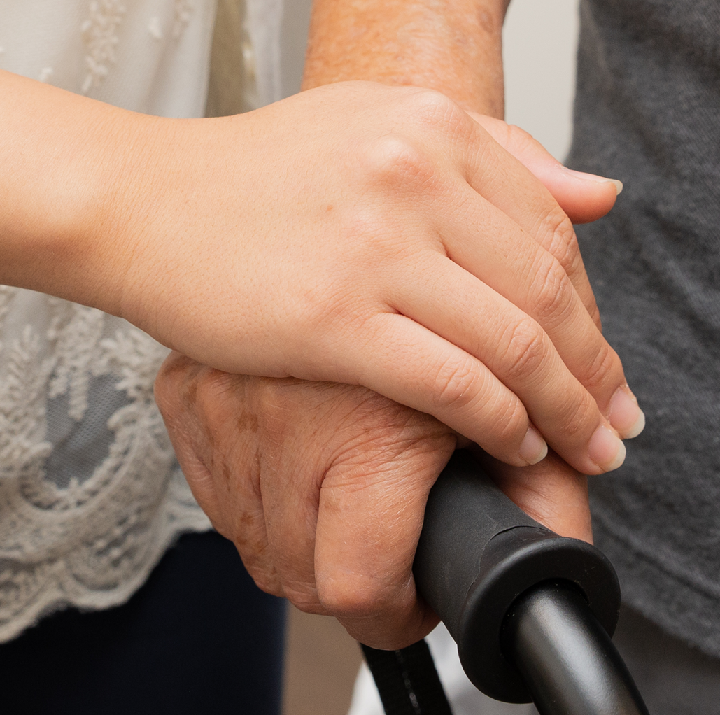 caregiving hands over older adult hand holding cane