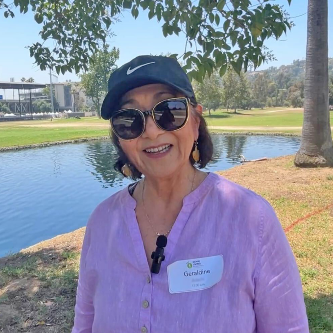 woman outside smiling wearing baseball cap, sunglasses, and pink shirt