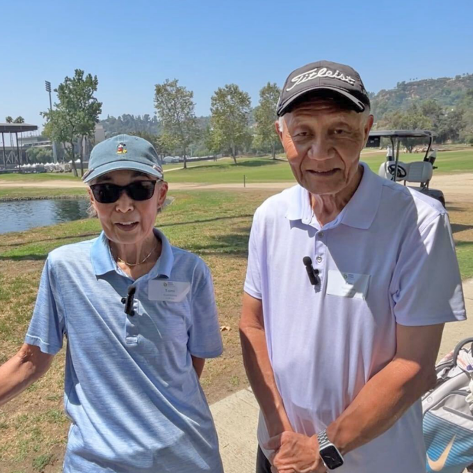 woman and man outside wearing baseball caps, golf cart in background