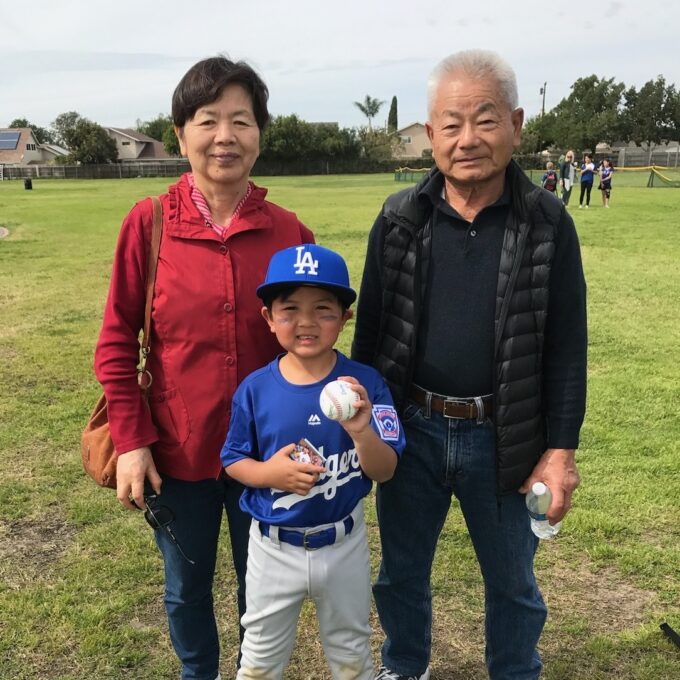 grandma nd grandpa standing with grandchild holding a baseball