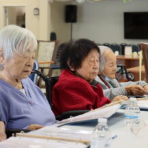 four women sitting at a table reading a from a binder