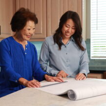 Beverly Ito and Desiree Kitagawa sitting at kitchen counter looking at site plans