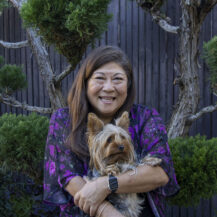 woman holding a dog while sitting in front of a tree