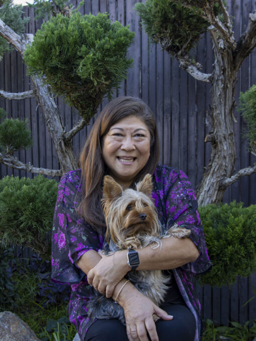 woman holding a dog while sitting in front of a tree
