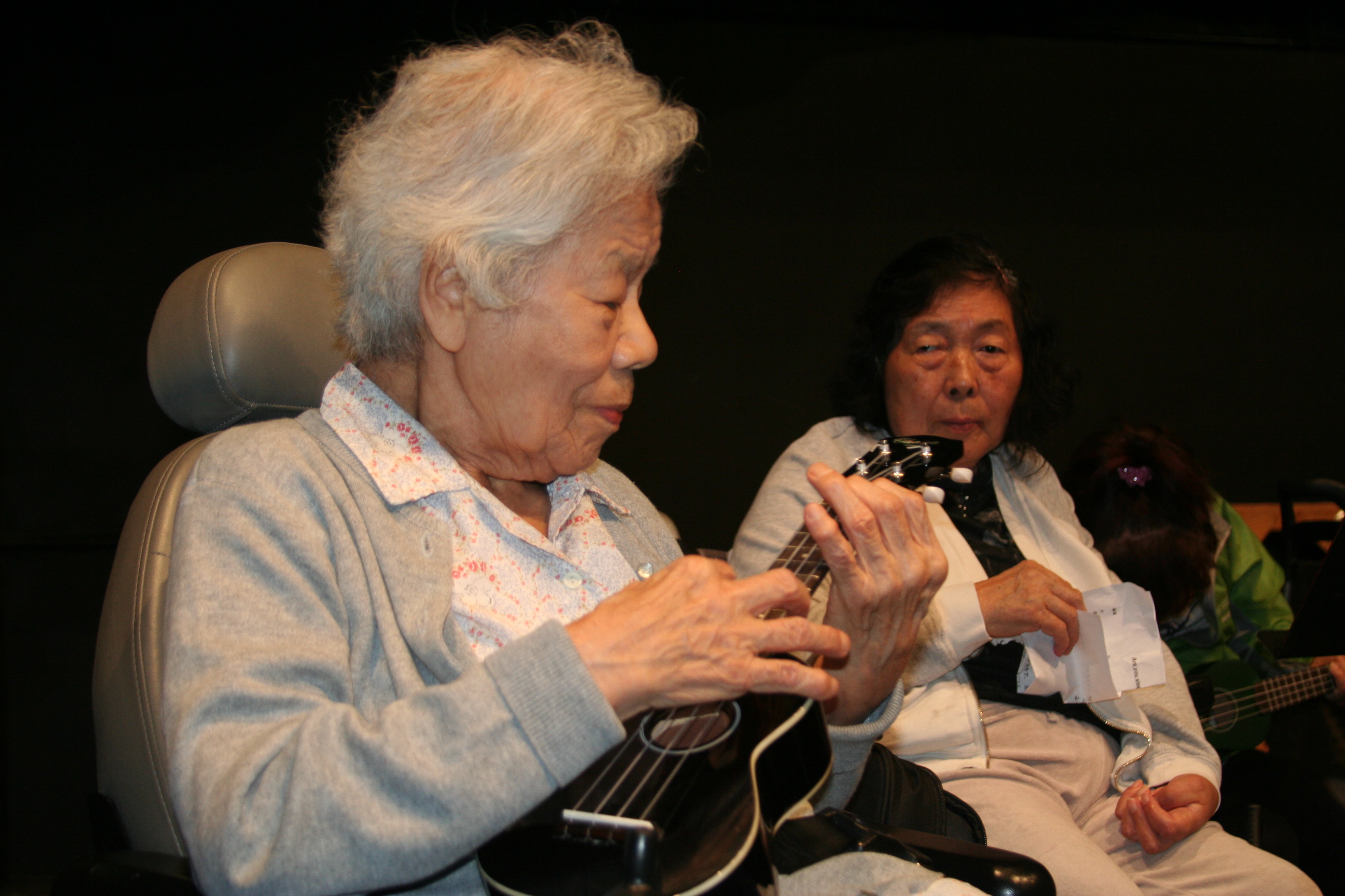 Older woman plays ukulele while another older woman watches.