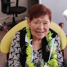 Older adult woman wearing a flower lei around her neck.