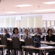 7 adults sitting at a table watching a presentation