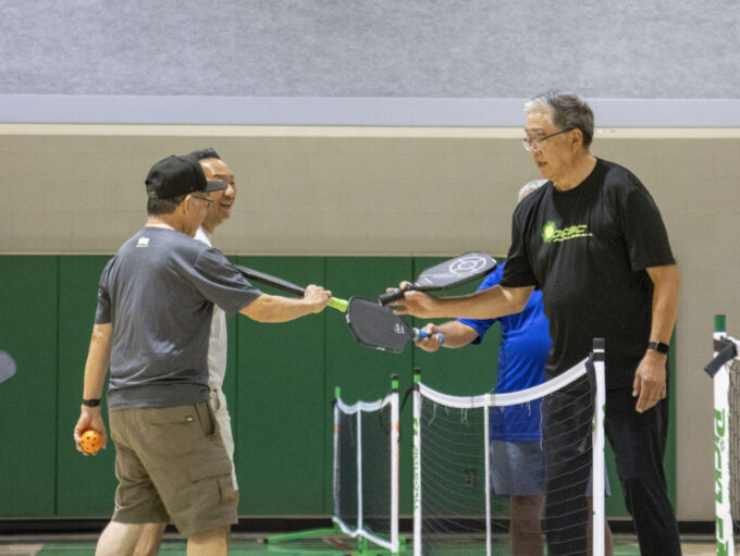 four people touching pickleball paddles together