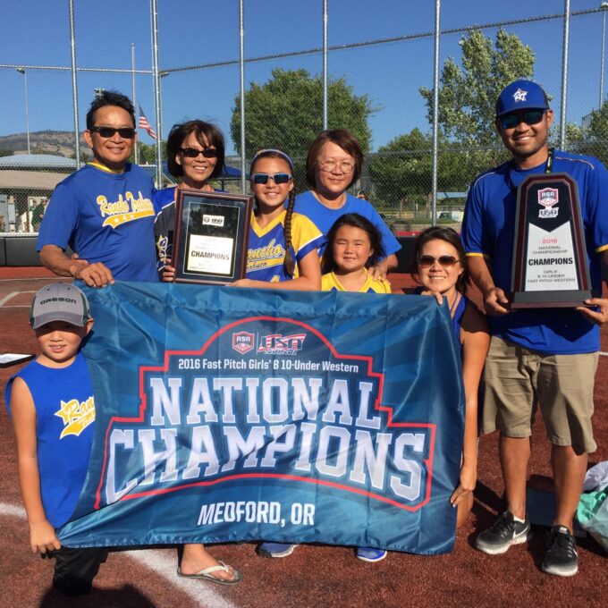 family smiling on softball field holding a sign that reads "National Champions"