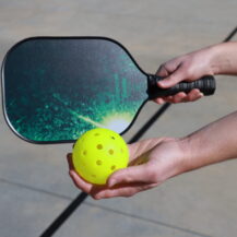 hands holding pickleball paddle and ball