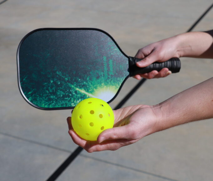 hands holding pickleball paddle and ball
