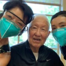 Two women with face masks on smiling with man