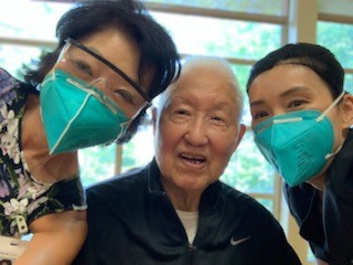 Two women with face masks on smiling with man