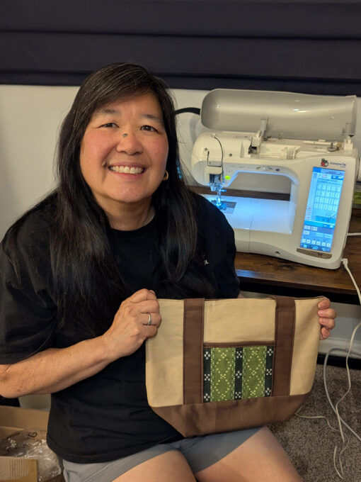 woman holding handmade bag with sewing machine in background