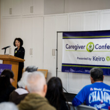 Beverly Ito talking at podium with Caregiver Conference banner in the back