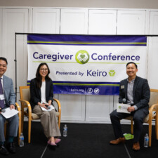 Tomohiro J. Kagami, Mei Kameda, and Makoto Kotani smiling on stage with Caregiver Conference banner in background