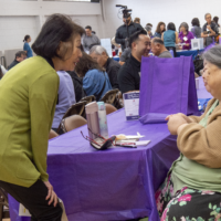 a woman in green talking with a woman sitting down in beige