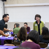 a man in black and a woman in green talking with people at a table