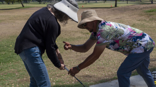 a man in a Hawaiian shirt helping a woman in black with golf