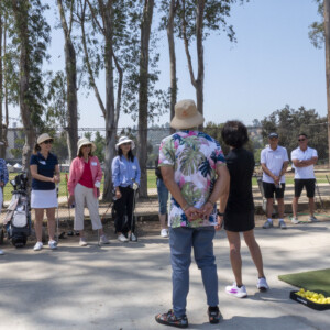 a woman in black standing next to a man in a Hawaiian shirt talking to a group of people