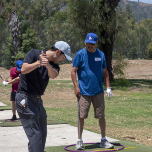 a man in black instructing to a man in blue on how to golf