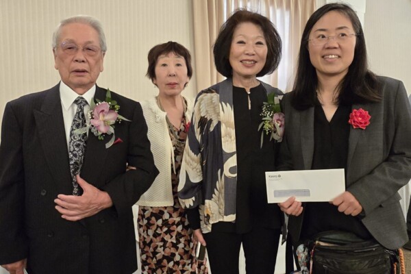 Four people smiling and one person is holding up a envelope