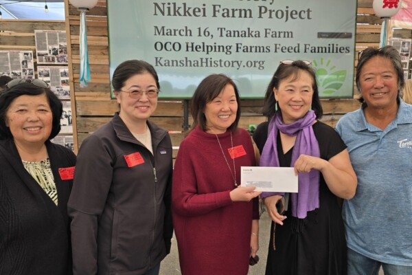 Five people smiling and two people are holding up a envelope