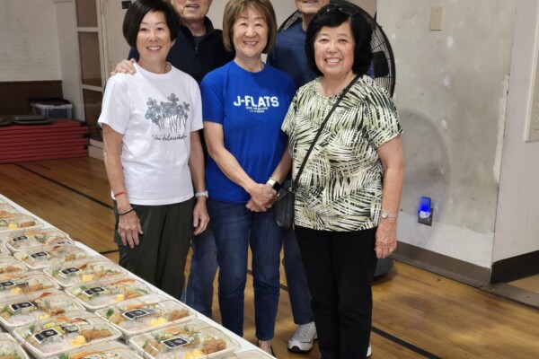 five people smiling with rows of bento on table