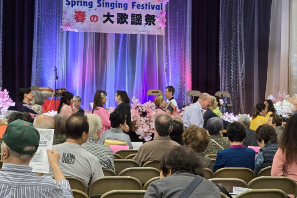 crowd sitting in front of stage with sign that reads "Spring Singing Festival"