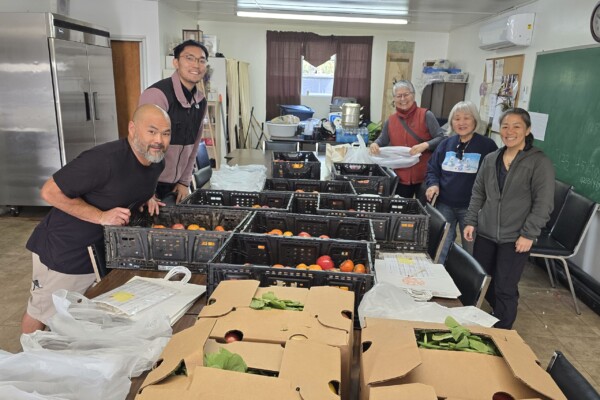 five people gathered around table holding baskets of produce