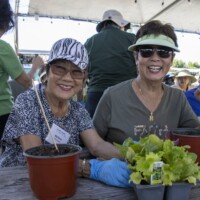 two woman smiling and holding plants