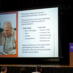 Takeshi talking by a podium with presentation slides