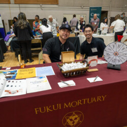 two men in back polos siling behind a red table