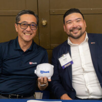 George Tanaka and Takeshi Yamada smiling with a piggy bank