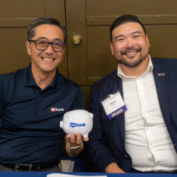 George Tanaka and Takeshi Yamada smiling with a piggy bank