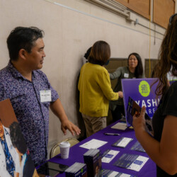 Dr Yanami in a purple button up standing by a purple table