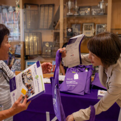 Yukari Roberts in a beige blazer giving a woman in blue striped shirt a purple bag