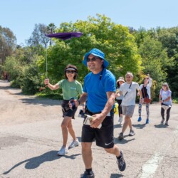 a man in blue and a woman in green with a purple flag walking and smiling