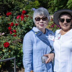 two women posing next to rose bushes