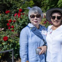two women posing next to rose bushes