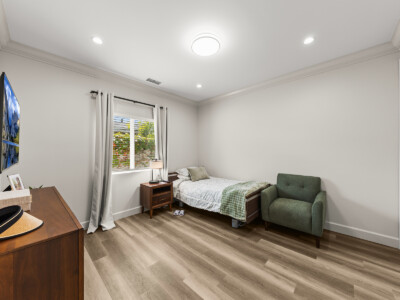 a bed with green comforter, green chair, wood dresser, and tv in a bedroom