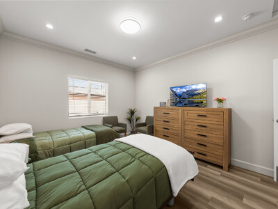 two beds with green comforters, wooden dresser, tv, in a bedroom